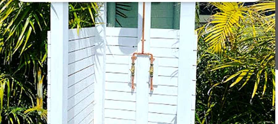 Outdoor copper pipework and valves mounted on white timber slats, with tropical planting either side.