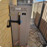 Outdoor hot water unit on a brick wall with copper pipe and a blue isolation valve.