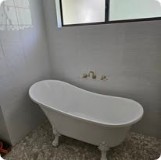 White freestanding clawfoot bathtub on a pebble floor, wall-mounted tapware.